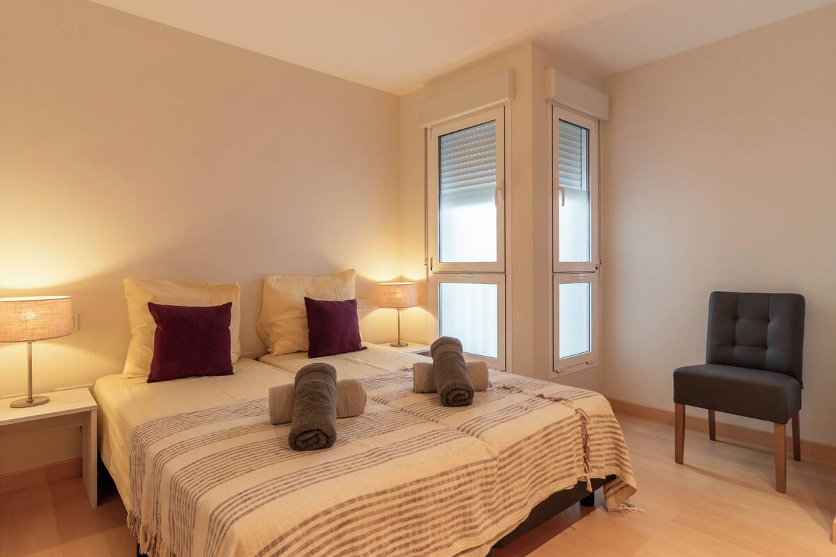 Une chambre à coucher avec un lit, deux lampes de chevet, une chaise et une fenêtre avec des stores.