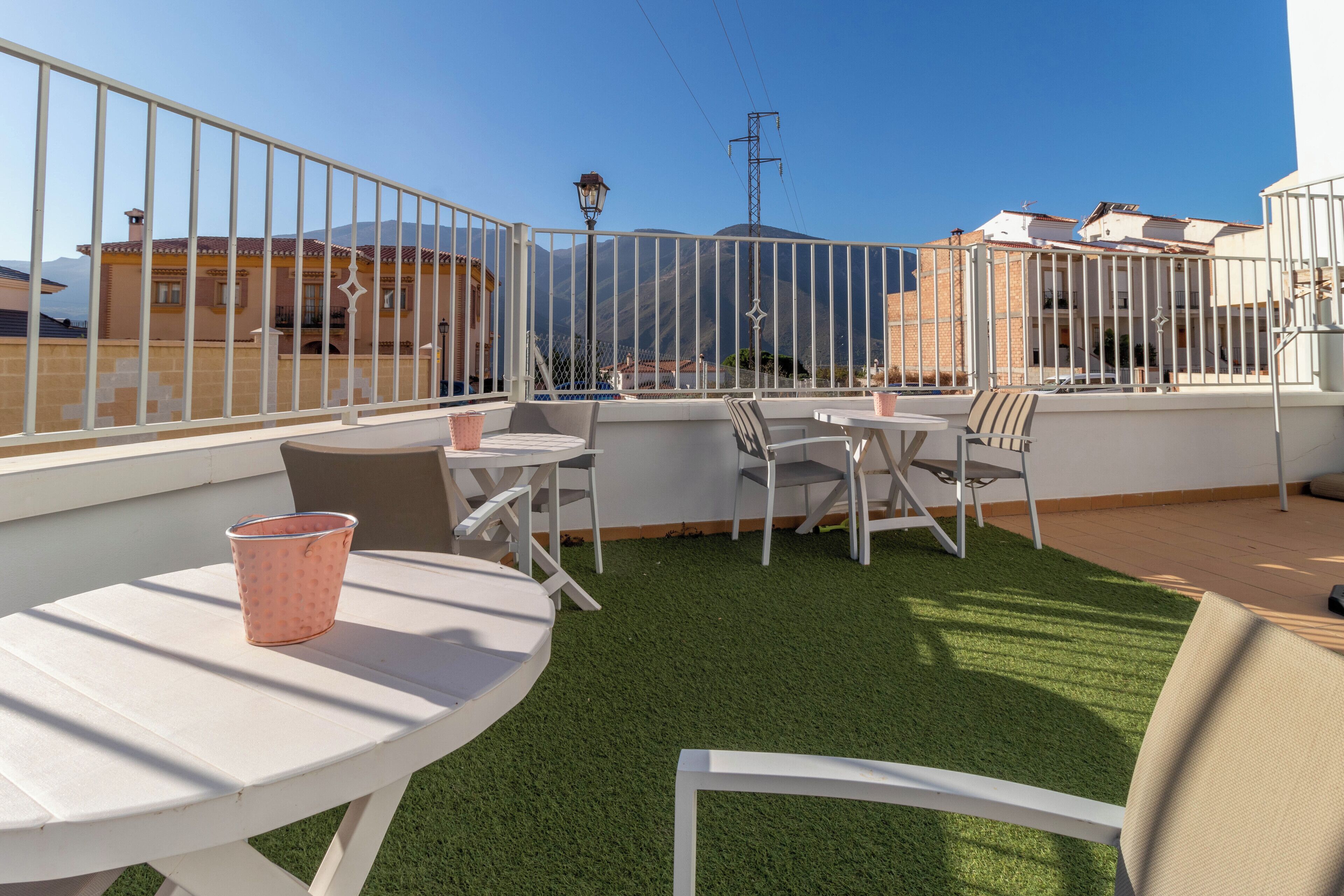 A rooftop terrace with a white fence, a table with chairs, and a small pink bucket.