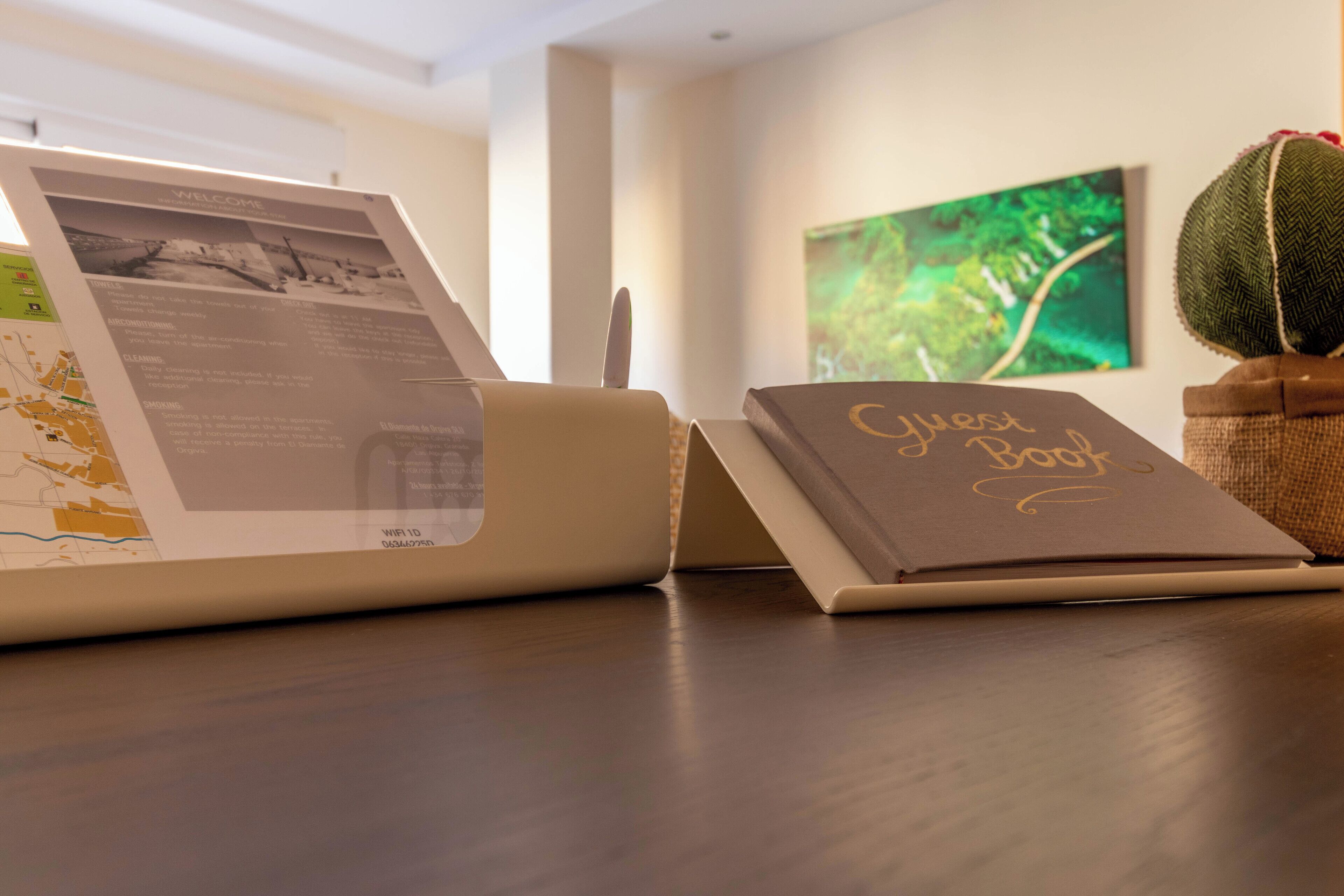 A brochure stand with a map and informational pamphlet, a notebook titled 'Guest Book', and a decorative plant on a wooden table.