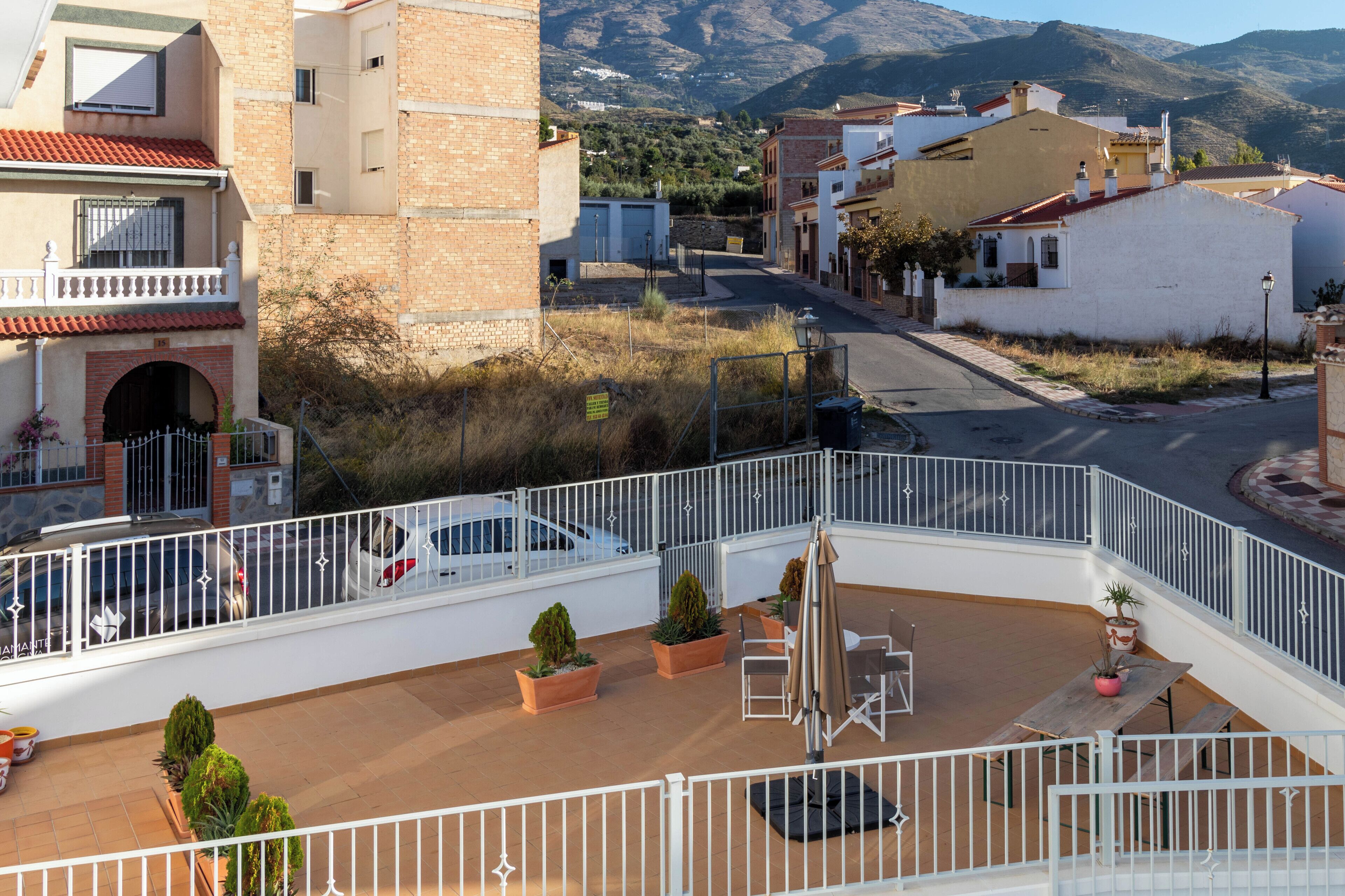 A rooftop terrace with outdoor seating, potted plants, and a view of a hillside town.