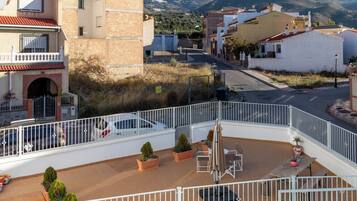 A rooftop terrace with outdoor seating, potted plants, and a view of a hillside town.