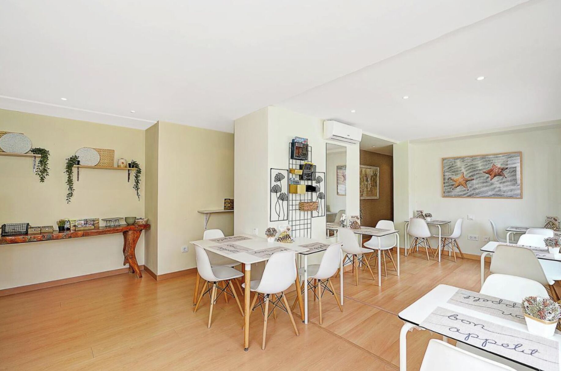 A spacious living area with a dining table and chairs, a kitchen area with a counter and shelves, and a hallway leading to another room.