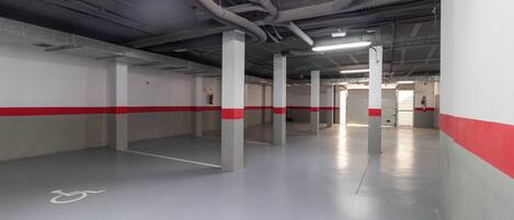 Un estacionamiento amplio y vacío con paredes blancas y rojas, pilares grises y un espacio para sillas de ruedas.