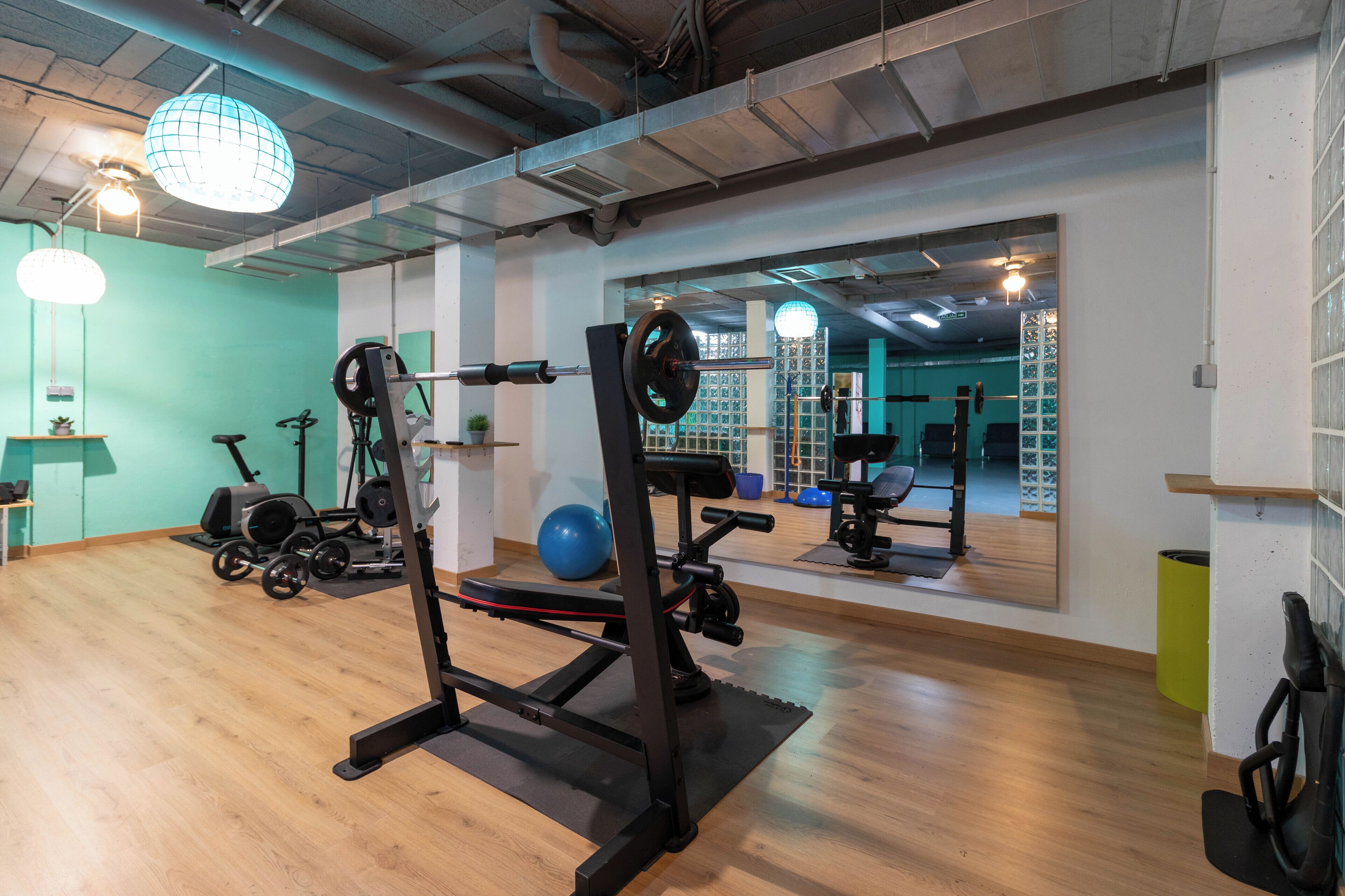 Ett gym med träningsutrustning, en vägg med speglar och ett trägolv.
