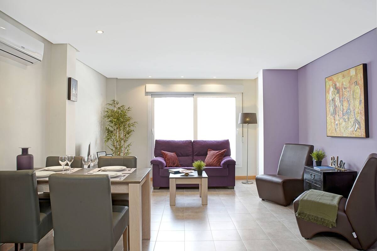 Un salon moderne comprenant un coin repas, un canapé violet, une table basse et une grande fenêtre.