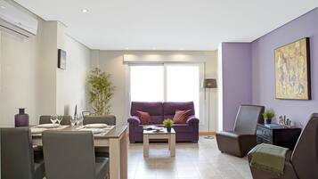 Una sala de estar moderna con comedor, un sofá morado, una mesa de centro y un ventanal grande.