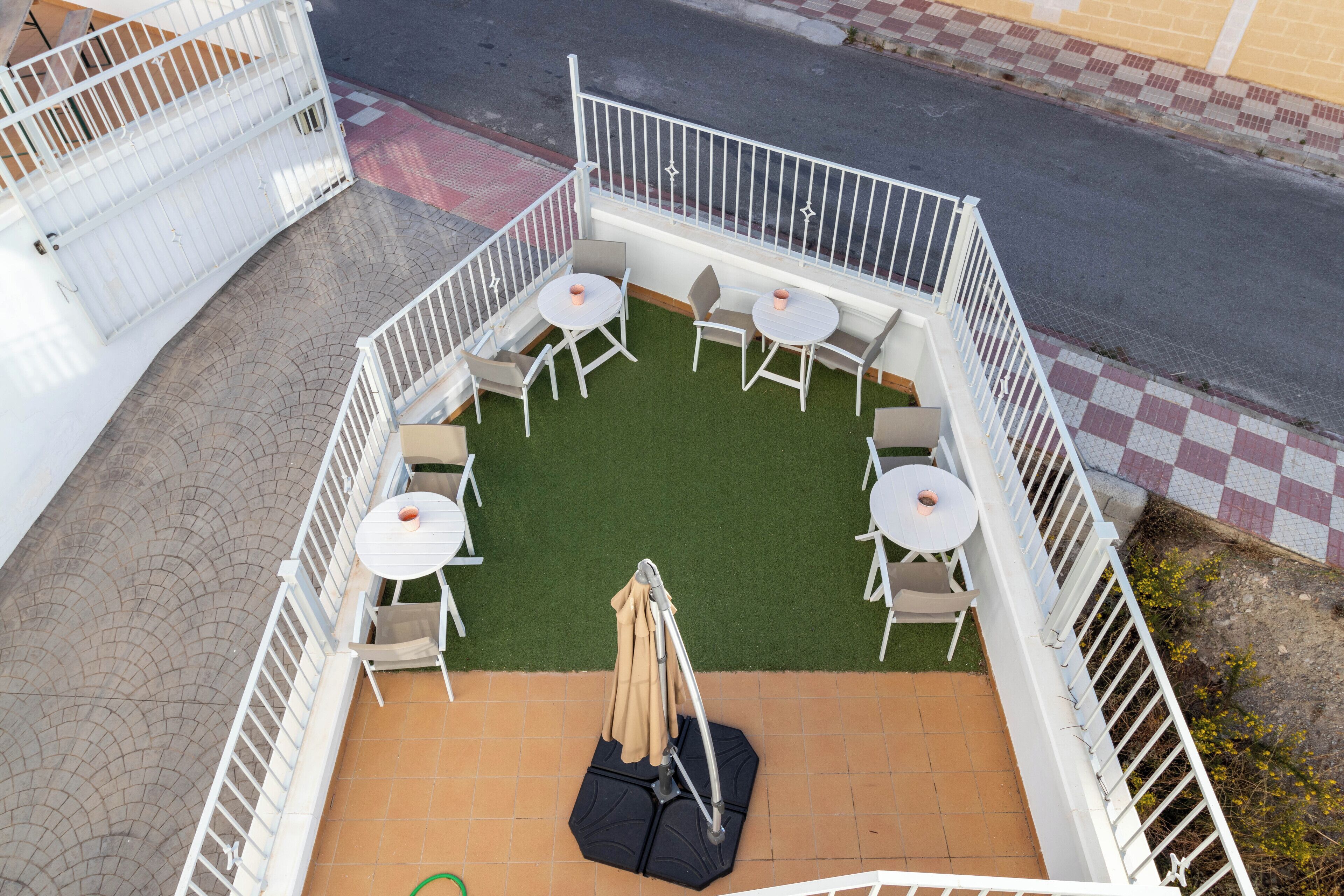 An outdoor patio with four round tables and chairs, a central umbrella, and a white railing.