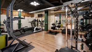 Een sportschool met diverse fitnessapparatuur, houten vloer en een spiegelwand.
