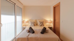 Een hotelkamer met een bed, twee bedlampen, een houten deur en een raam met jaloezieën.