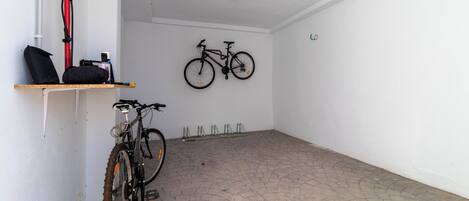 Una habitación limpia y vacía con piso de baldosas, una bicicleta colgada en la pared y un estante con una bolsa y un objeto rojo.