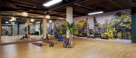 A spacious indoor area with wooden flooring, exercise equipment, and a mural of a temple.