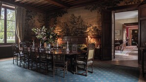 A formal dining room with a large wooden table and chairs, a vase of flowers, and a mural on the wall. - Château Sénéjac (Le Pian-Medoc)