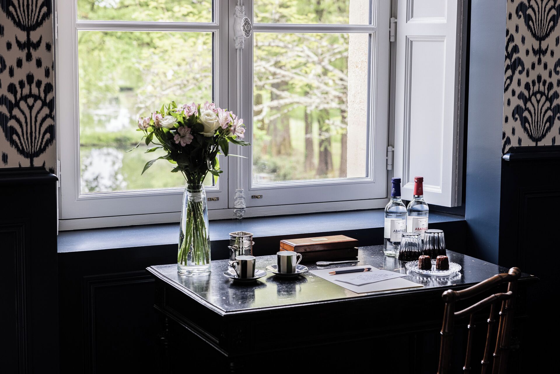 Ein Tisch mit einer Blumenvase, zwei Flaschen, einer Tasse, einem Untertasse, einer Teekanne und einem Teller mit Desserts.