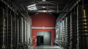 A large industrial space with rows of stainless steel tanks, a red wall, and a door at the end.
