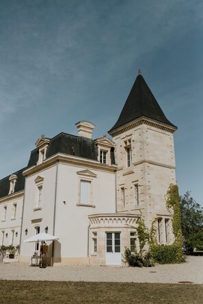 A large, historic building with a prominent tower, a courtyard, and a small outdoor seating area. - Château Sénéjac (Le Pian-Medoc)