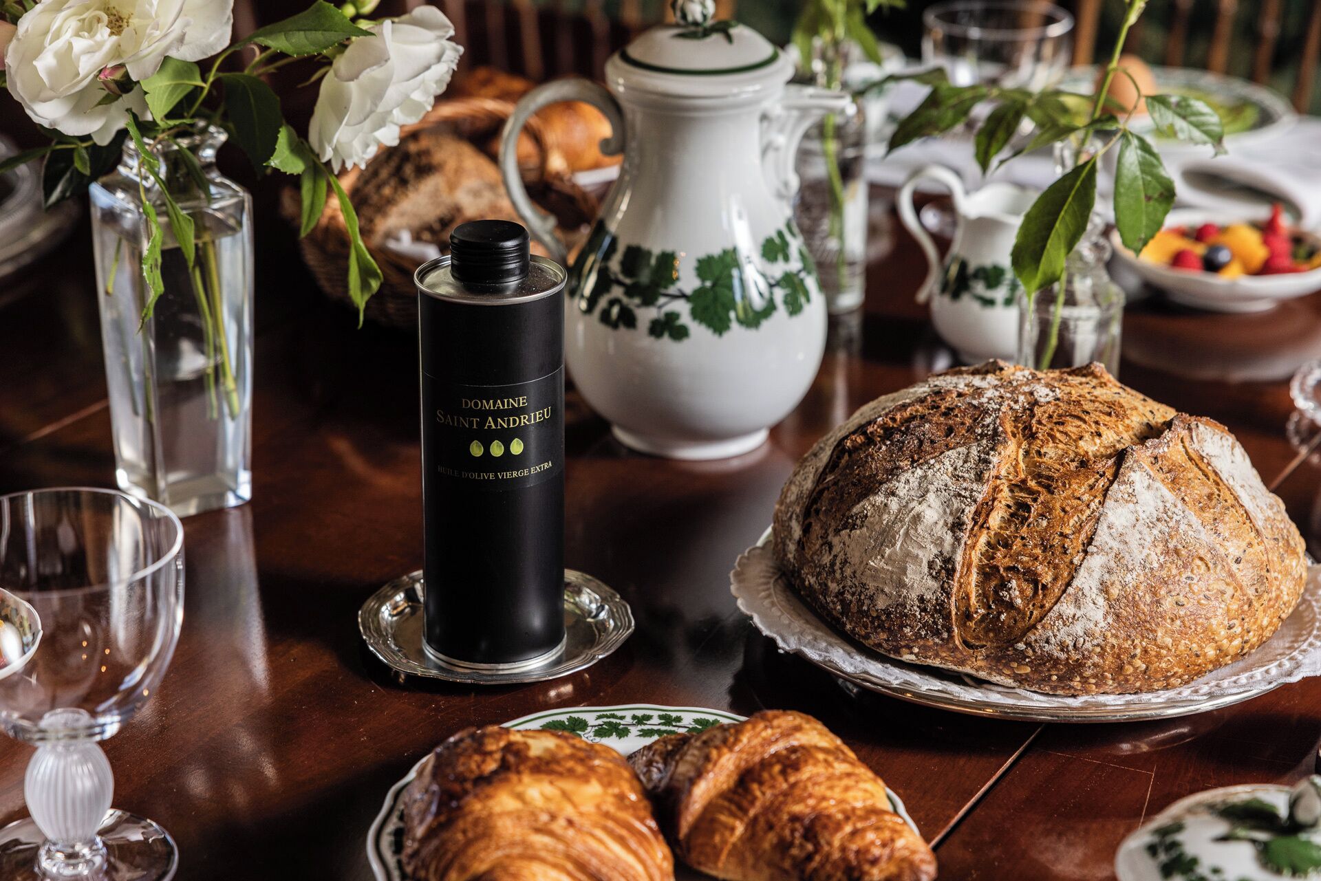 A dining table with a variety of food items, including bread, pastries, and a bottle of Domaine Saint Andreu wine.