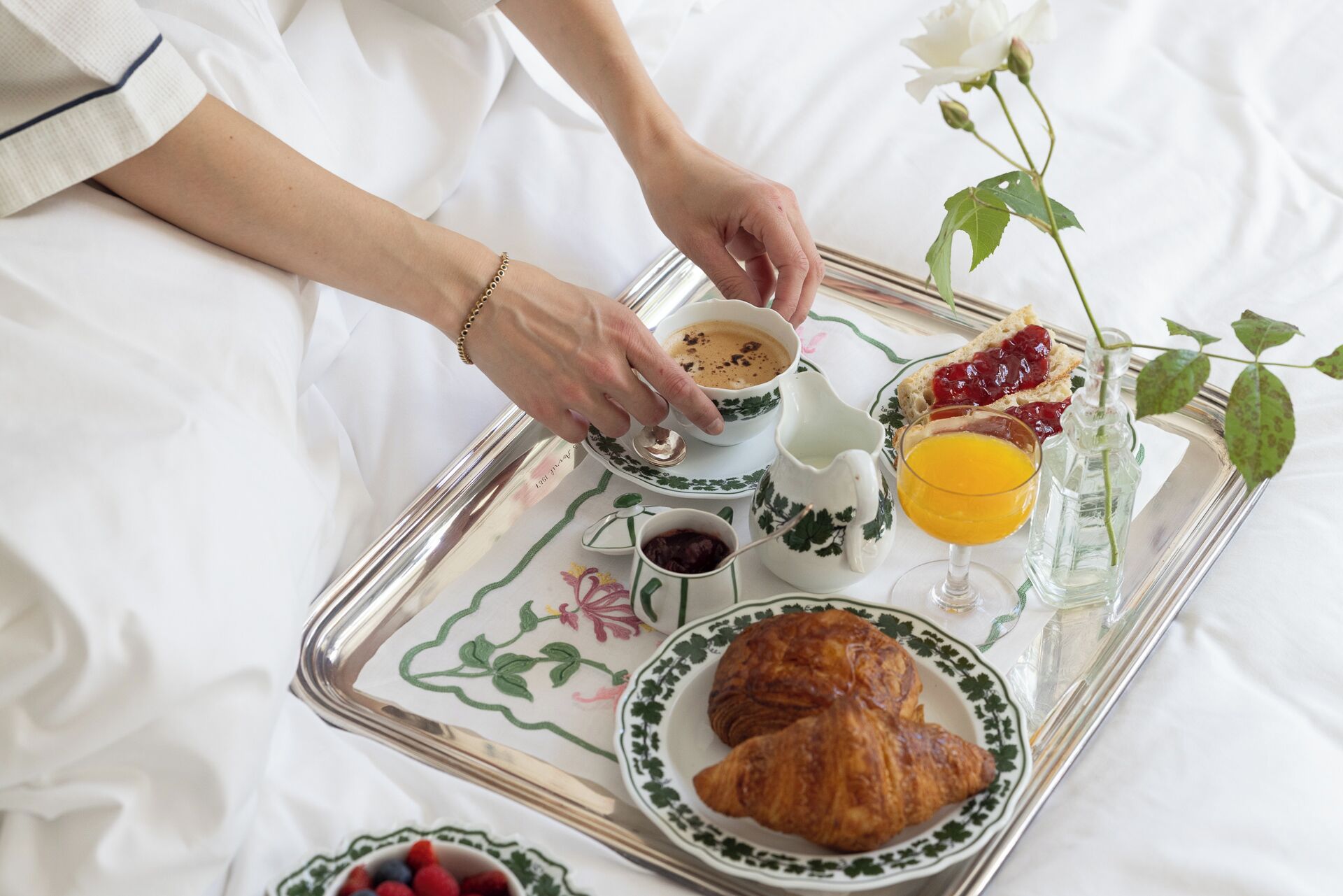 A breakfast tray with croissants, a cup of coffee, jam, and a glass of orange juice.
