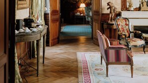 A room with a wooden floor, a patterned rug, a bench, a table with a lamp, and a statue. - Château Sénéjac (Le Pian-Medoc)