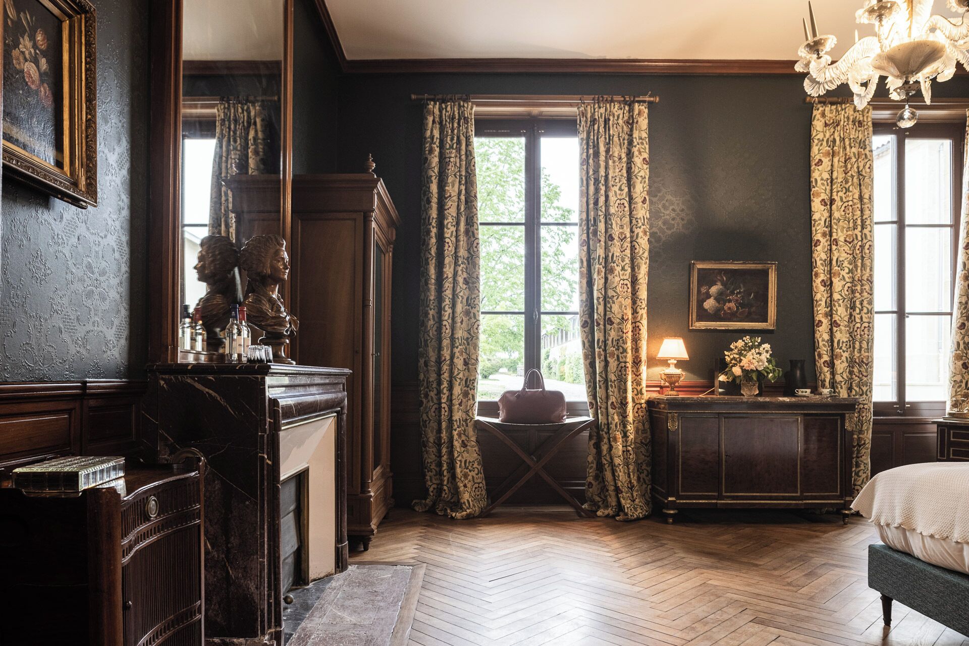 Una habitación con un ventanal grande, un escritorio con lámpara, una cama y un candelabro.