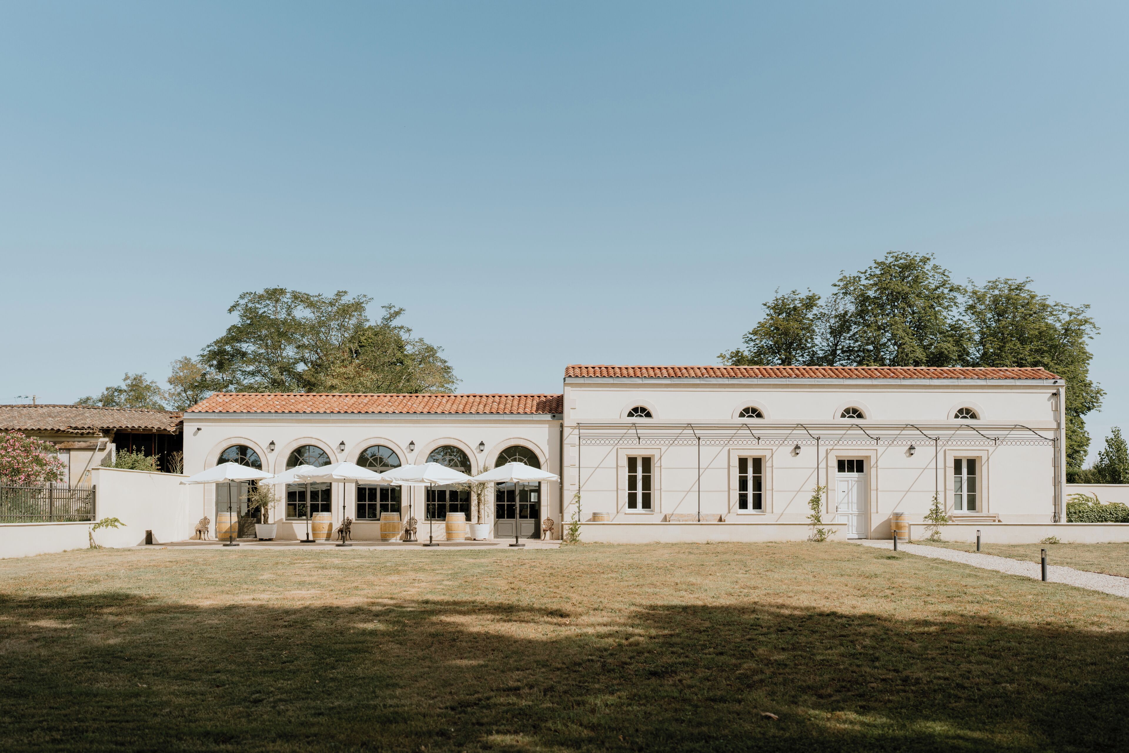 A white building with a tiled roof, arched windows, and outdoor seating with umbrellas.