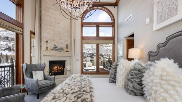 A spacious living room with a fireplace, a large window with a view of a snowy landscape, and a cozy seating area with a fur throw. - Luxury Ritz-Carlton Condo W/Views (Vail)