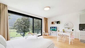 Ein modernes Hotelzimmer mit einem großen Bett, einem Schreibtisch mit Fernseher und Blick auf eine grüne Landschaft.