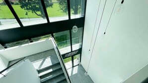 Eine moderne Treppe mit Glasgeländern und Blick auf eine grüne Außenanlage.