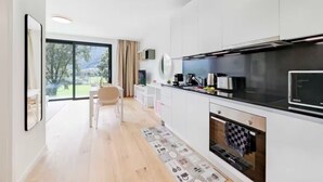 Eine moderne Küche mit weißen Schränken, einer schwarzen Arbeitsplatte und einem großen Fenster mit Blick auf einen Garten.