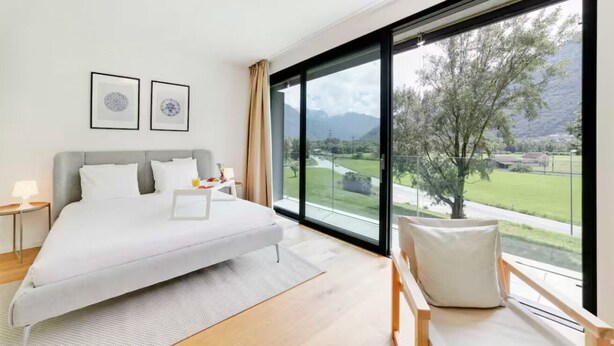 Ein modernes Schlafzimmer mit einem großen Bett, Blick auf eine grüne Landschaft und zwei gerahmte Bilder an der Wand.