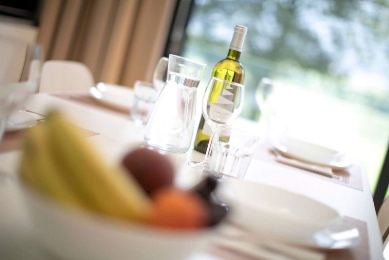 Une table à manger avec une bouteille de vin blanc, des verres et une assiette de fruits.