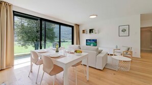 Ein modernes Wohnzimmer mit Essbereich, großen Fenstern, einem Flachbildfernseher und einer gemütlichen Sitzecke.