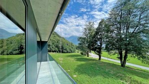Ein modernes Gebäude mit großen Glasfenstern und Blick auf eine üppige, gr üne Landschaft mit Bäumen und einer Straße.