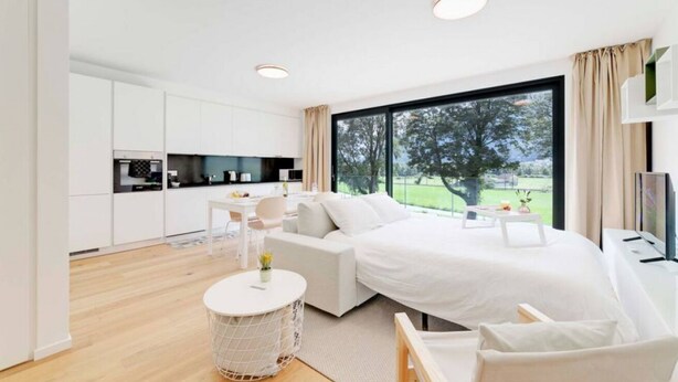 Ein modernes Schlafzimmer mit einem großen Bett, einem kleinen Schreibtisch und Gartenblick durch ein großes Fenster.