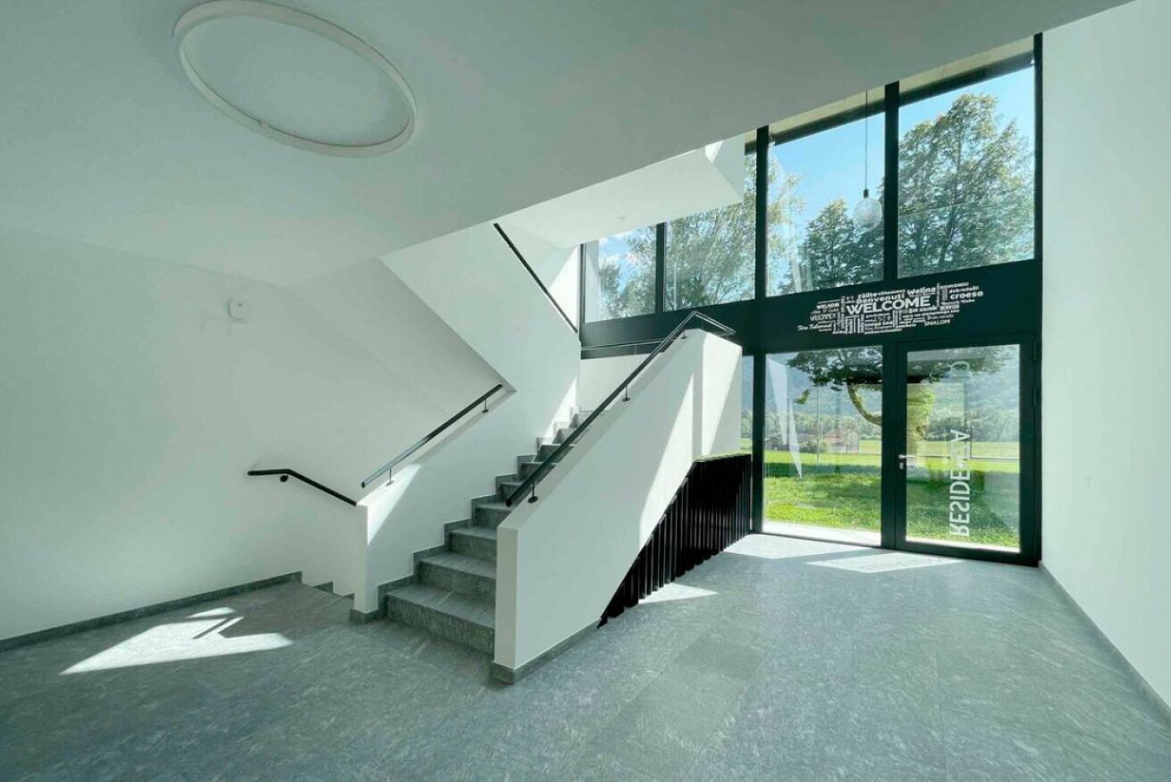 Ein modernes Interieur mit Treppe, großen Fenstern und einem einladenden Schild.