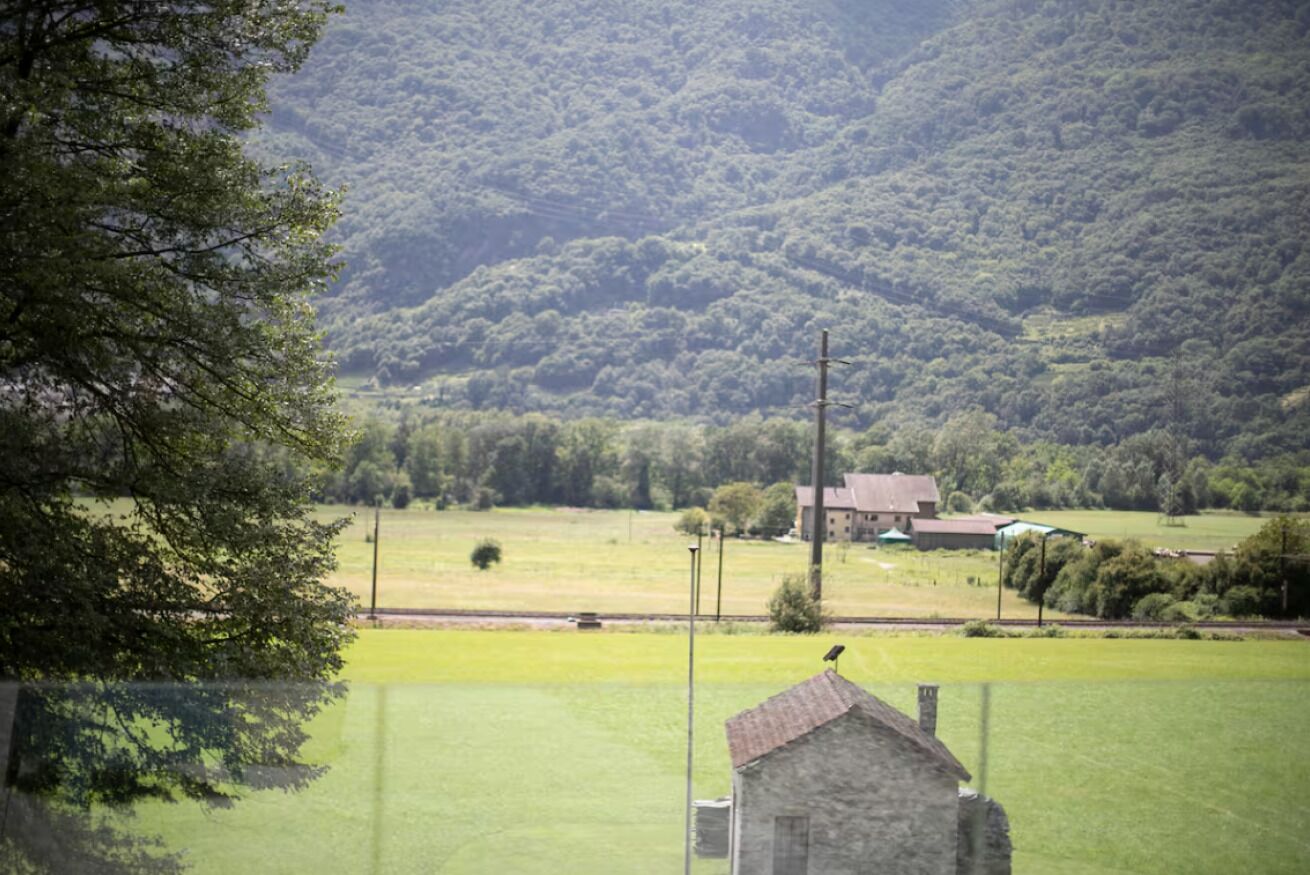 A rural landscape with a stone building, a fenced field, and a hill in the background.