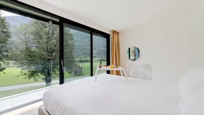 A modern hotel room with a large bed, a small table with a drink, and a view of a green landscape through large windows. - An oasis of peace in nature (PPegasus 11 Residenza Ticino) (Bellinzona)