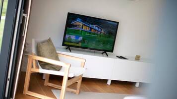 Una habitación con una televisión mostrando una casa, un mueble blanco y una silla de madera.