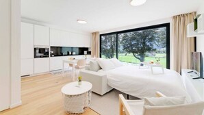 A modern bedroom with a large bed, a small desk, and a view of a garden through a large window. - An oasis of peace in nature (Perseo 02 Residenza Ticino) (Bellinzona)