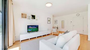 Una sala de estar moderna con un sofá blanco, un televisor de pantalla plana, un mueble blanco para entretenimiento y un ventanal grande.