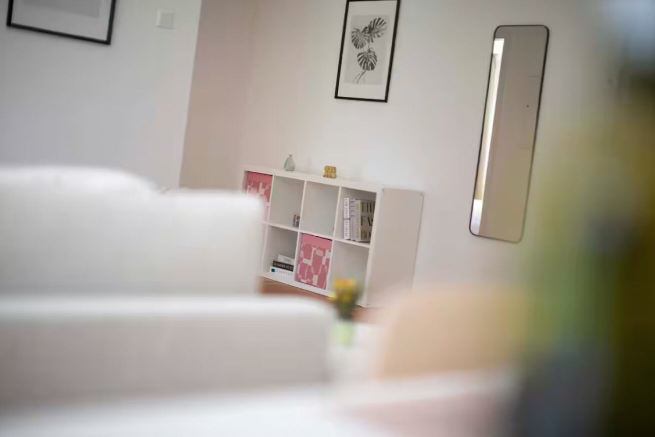 Ein modernes Wohnzimmer mit einem weißen Sofagarnitur, einem weißen Bücherregal und einem gerahmten Kunstwerk an der Wand.
