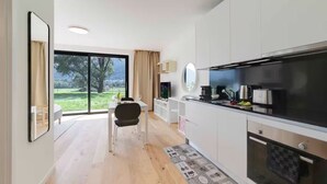 A modern kitchen with a large window, a dining area with a table and chairs, and a view of a green landscape. - An oasis of peace in nature (Auriga 04 Residenza Ticino) (Bellinzona)