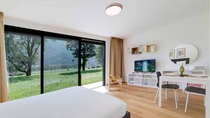A modern hotel room with a large bed, a desk with a TV, and a view of a green landscape through large windows. - An oasis of peace in nature (Auriga 04 Residenza Ticino) (Bellinzona)