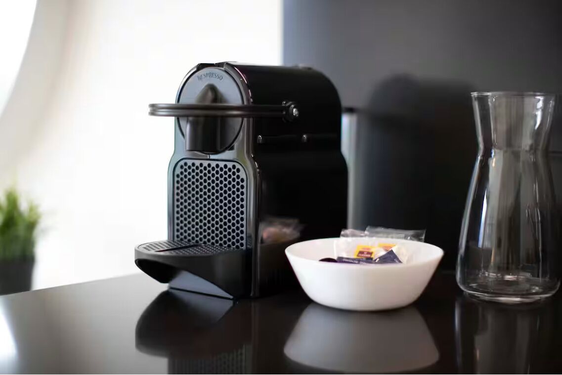 A coffee maker, a bowl with coffee pods, and a glass on a table.