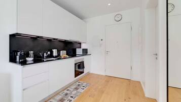 A modern kitchen with white cabinets, a black countertop, and a wooden floor.