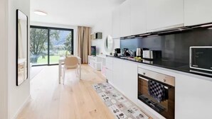A modern kitchen with white cabinets, a black countertop, and a large window overlooking a garden. - An oasis of peace in nature (Cassiopea 13 Residenza Ticino) (Bellinzona)