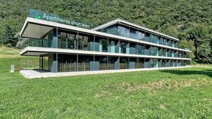 A modern multi-story building with a flat roof and large glass windows, labeled "Apartments short term." - An oasis of peace in nature (Cassiopea 13 Residenza Ticino) (Bellinzona)