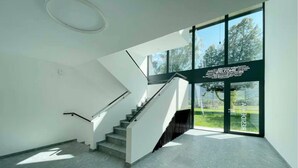 A modern interior with a staircase, large windows, and a welcoming sign. - An oasis of peace in nature (Cassiopea 13 Residenza Ticino) (Bellinzona)