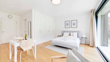 A modern bedroom with a bed, bedside tables, a desk with a chair, and a large window.