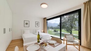 A modern hotel room with a large window, a dining area, and a bed. - An oasis of peace in nature (Sirio 09 Residenza Ticino) (Bellinzona)