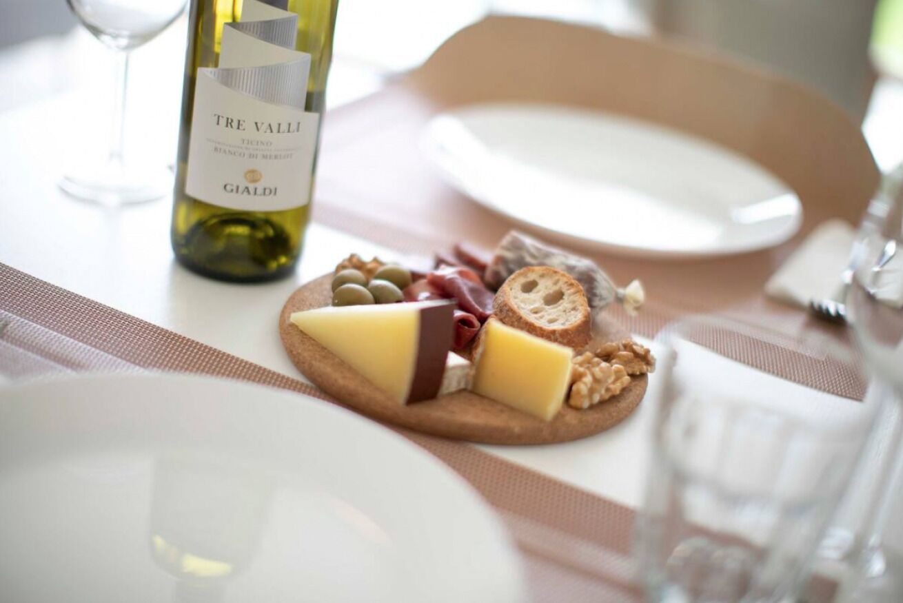 Une table dressée avec une bouteille de vin Tre Valli, une assiette de fromage, des noix et du pain.